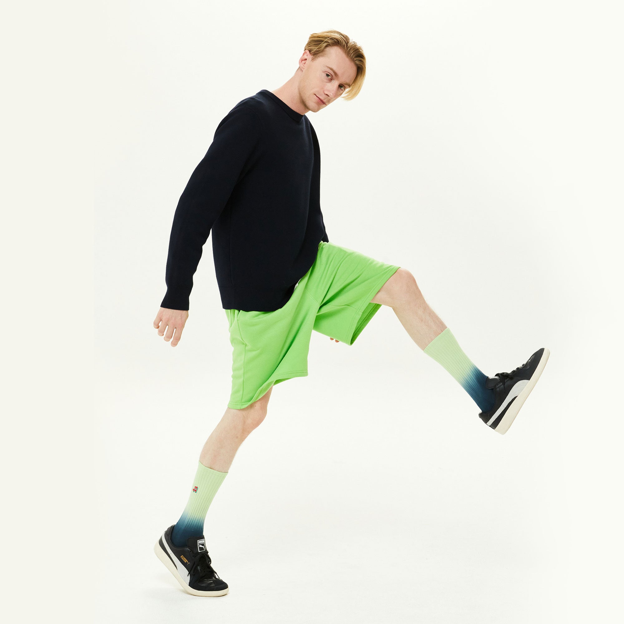 A man in black shirt and green shorts kicking a soccer ball.