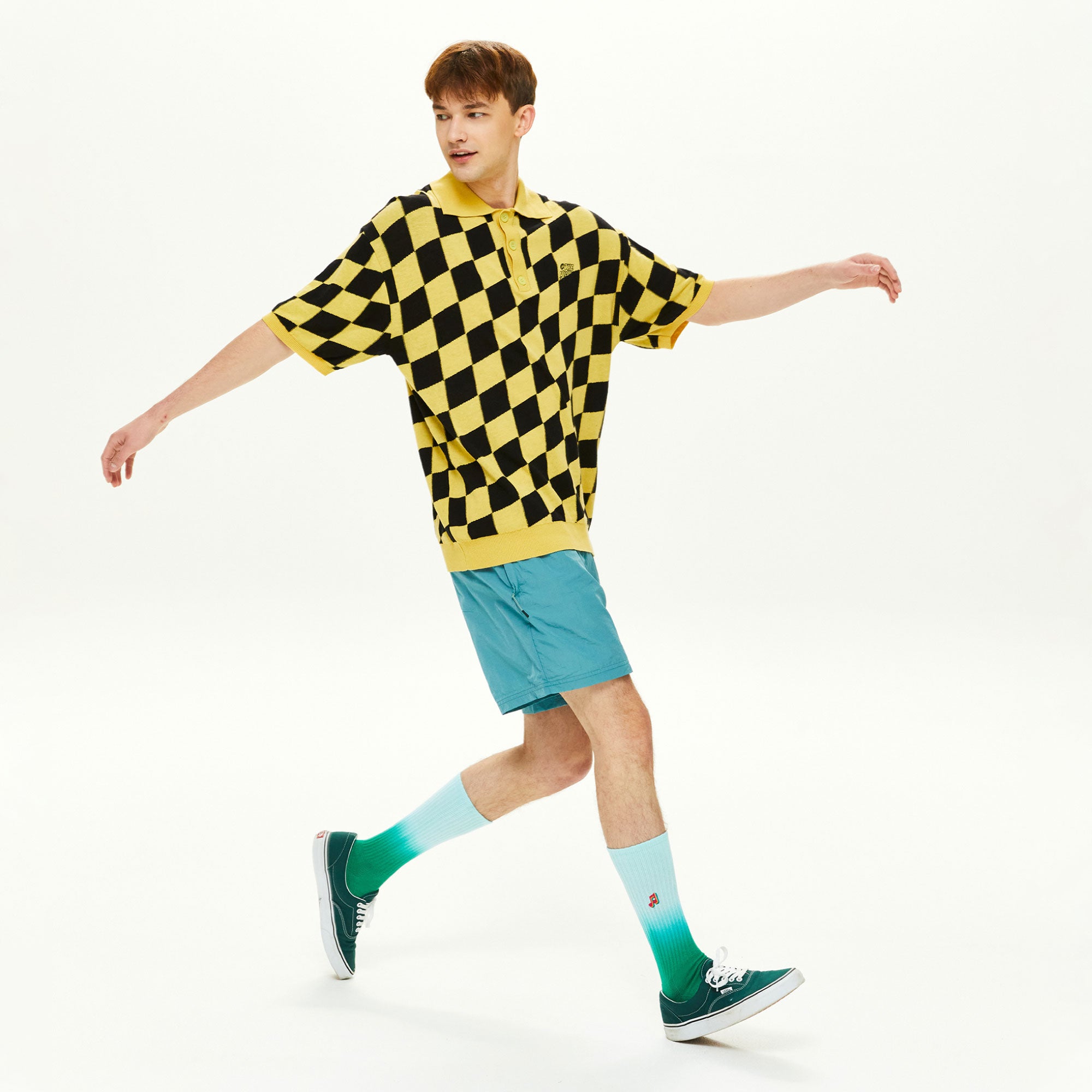 A man in a yellow and black checkered shirt is skateboarding.