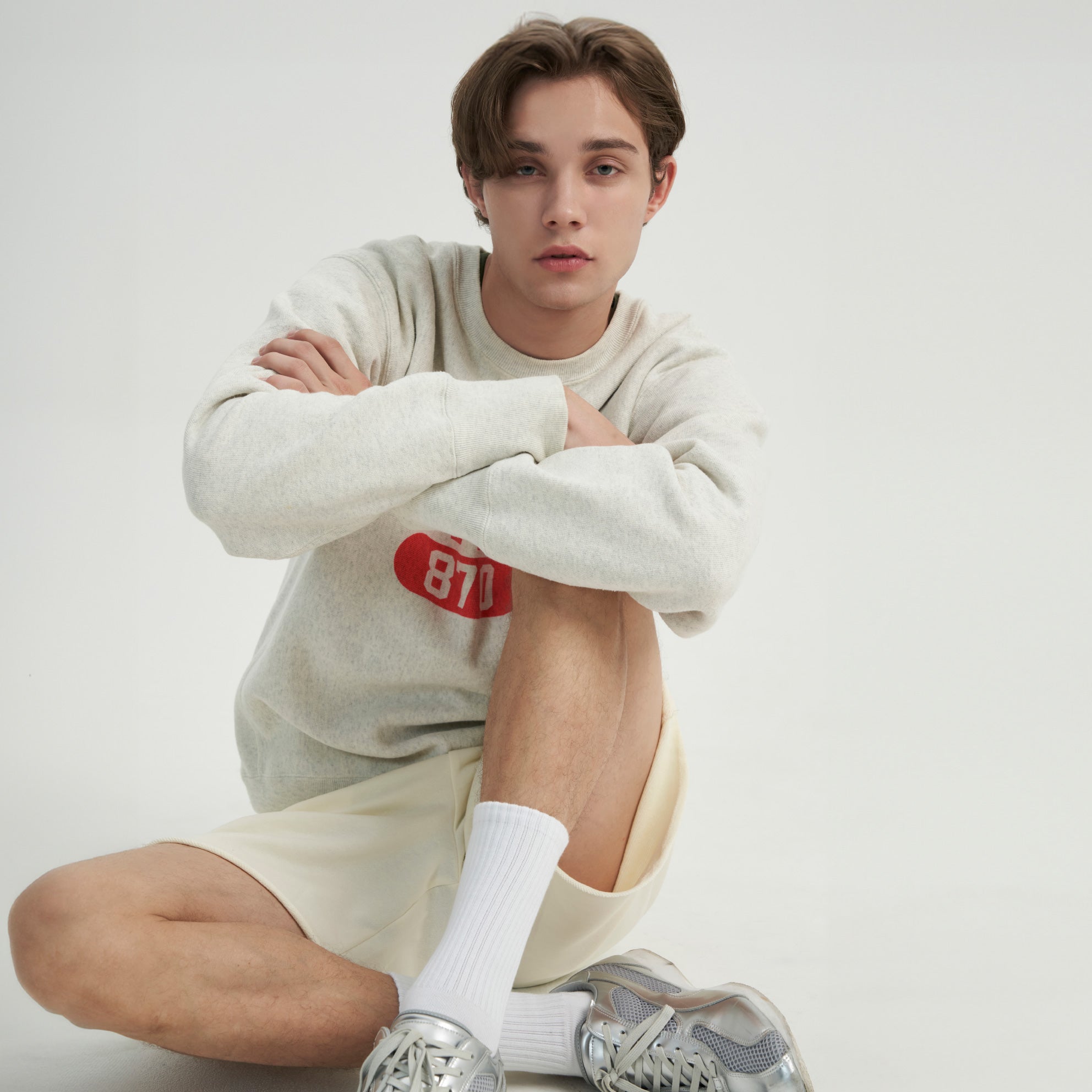 A young man sitting on the ground with his arms crossed.