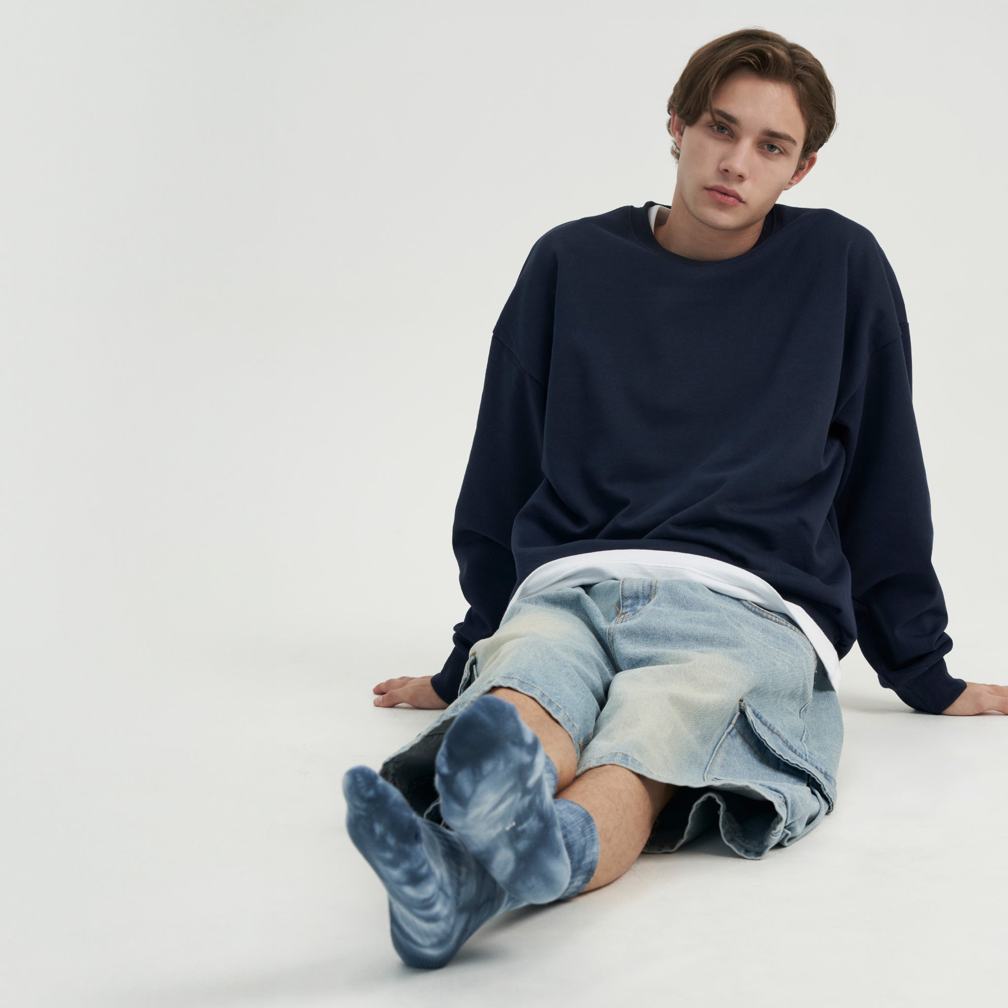 A young man sitting on the ground with his legs crossed.