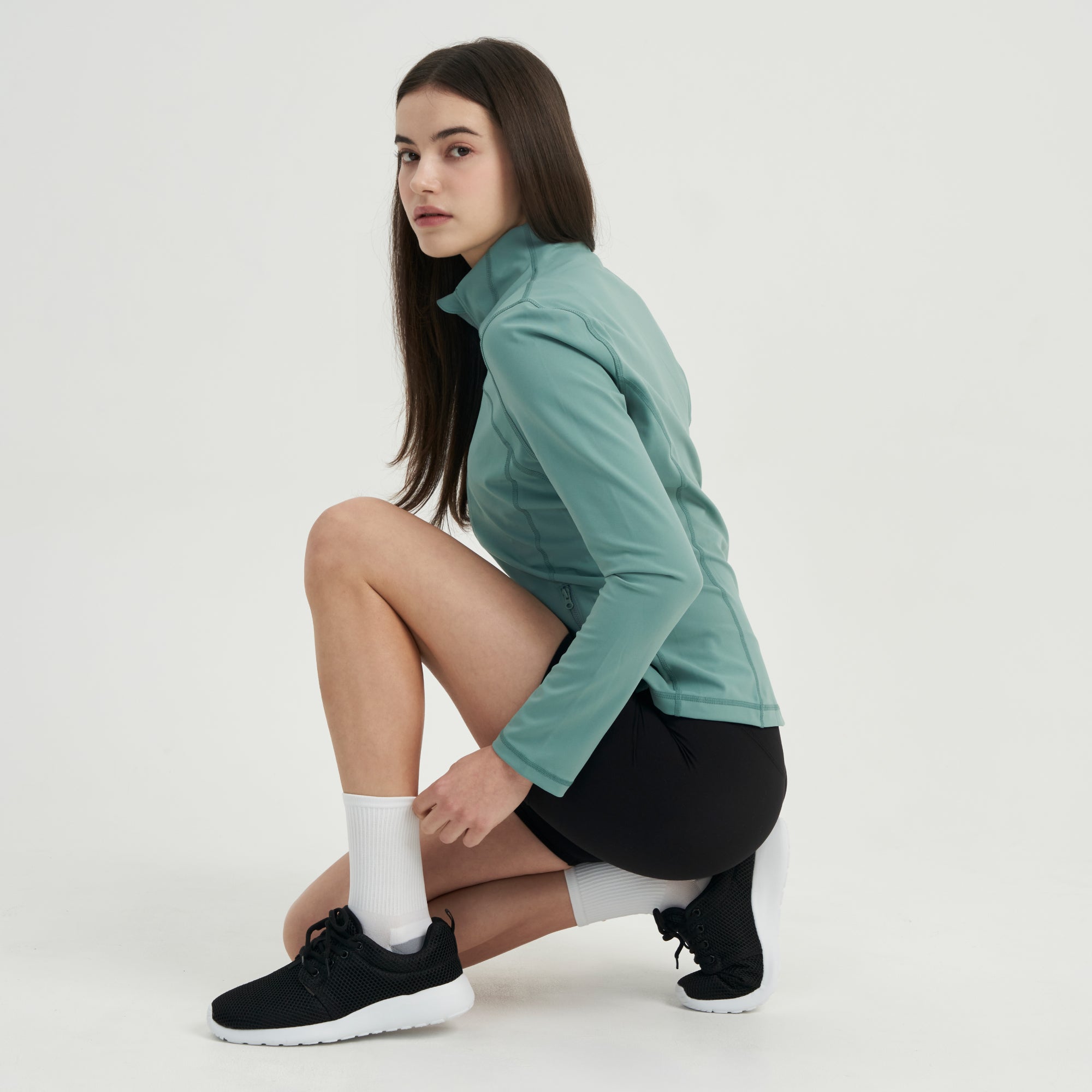 A woman in a green jacket and black shorts.