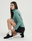A woman in a green jacket and black shorts.