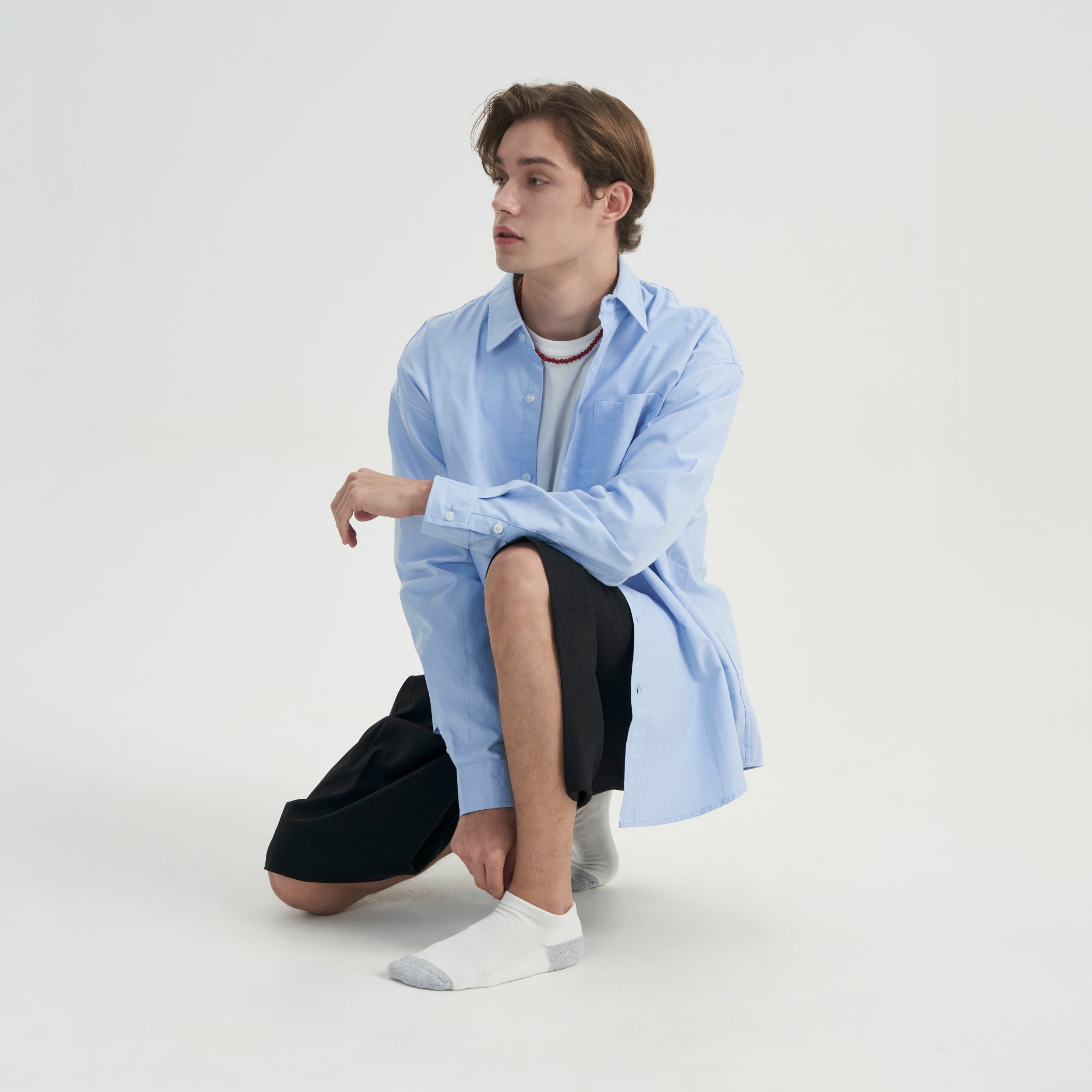 A young man sitting on the ground wearing a blue shirt and black pants.