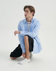 A young man sitting on the ground wearing a blue shirt and black pants.