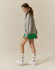 A woman in a grey sweatshirt and green shorts.