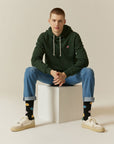 A man sitting on a stool wearing a green hoodie.