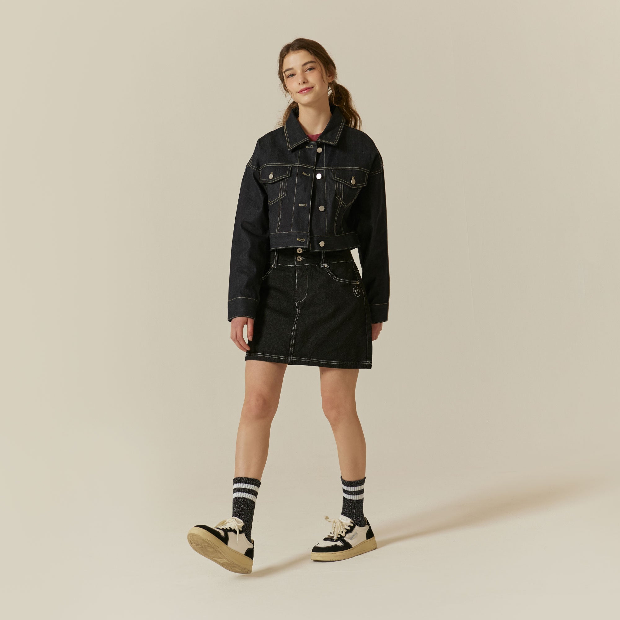 A woman in a black denim jacket and skirt.
