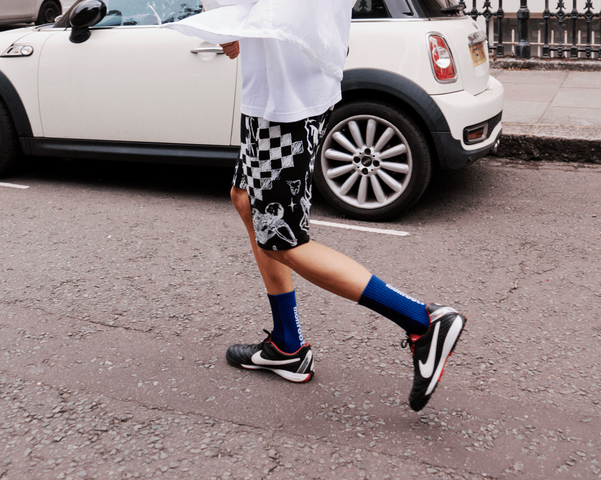 A man walking across a parking lot next to a white car.