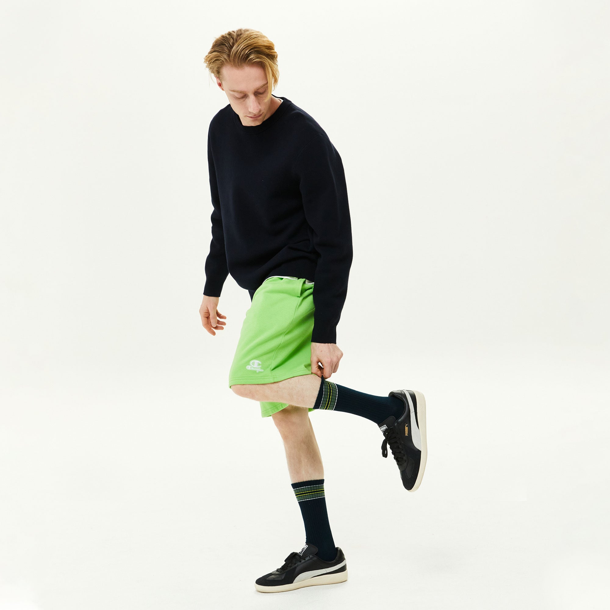 A man in black shirt and green shorts kicking a soccer ball.