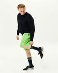 A man in black shirt and green shorts kicking a soccer ball.