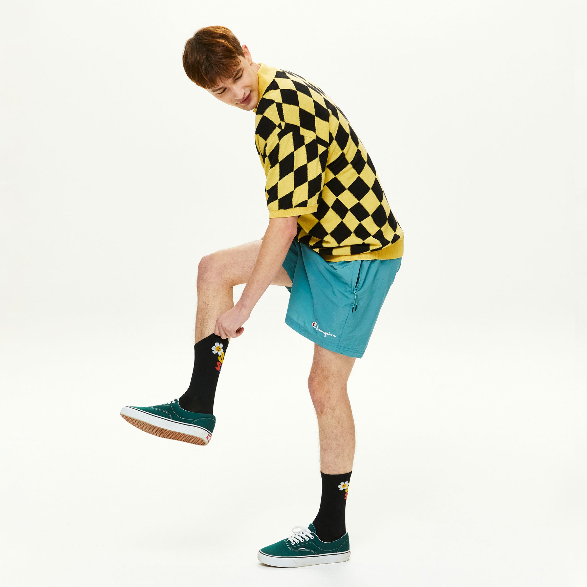 A man in a yellow and black checkered shirt doing a trick on a skate.