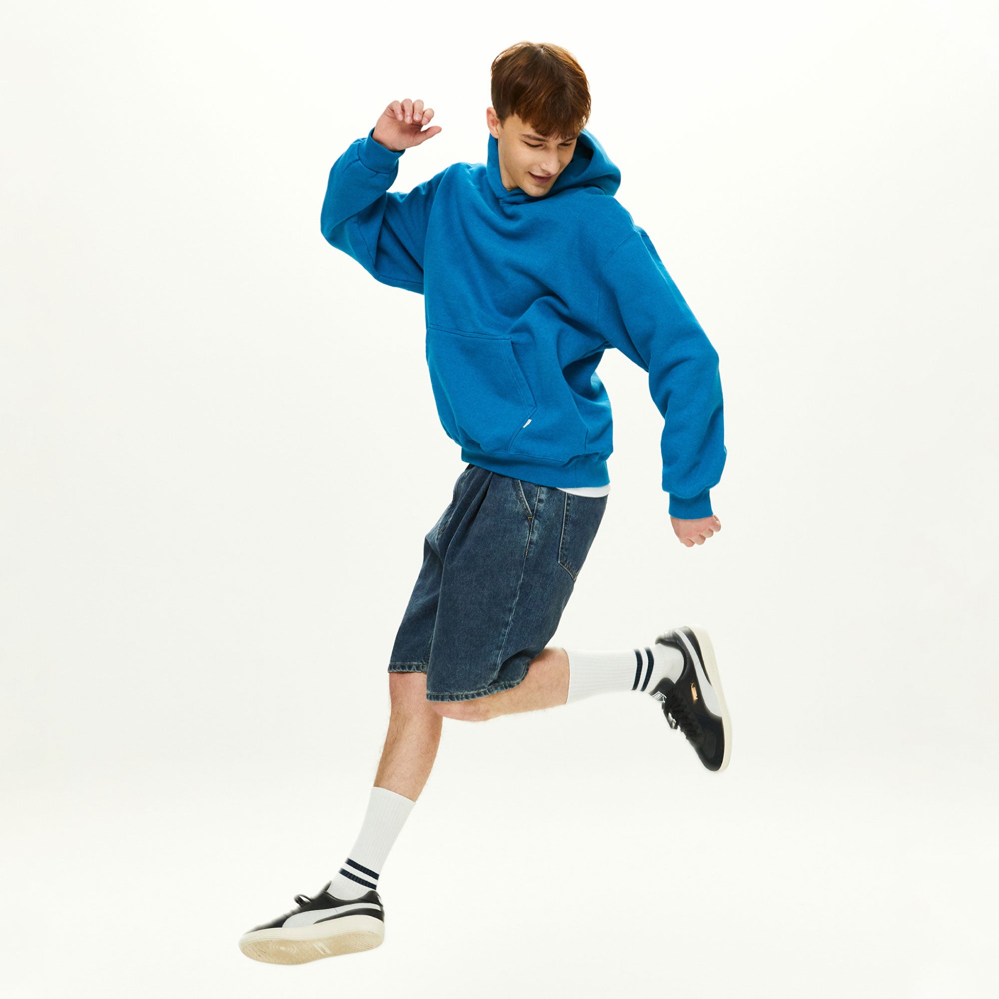 A young man in a blue hoodie is jumping in the air.