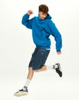 A young man in a blue hoodie is jumping in the air.