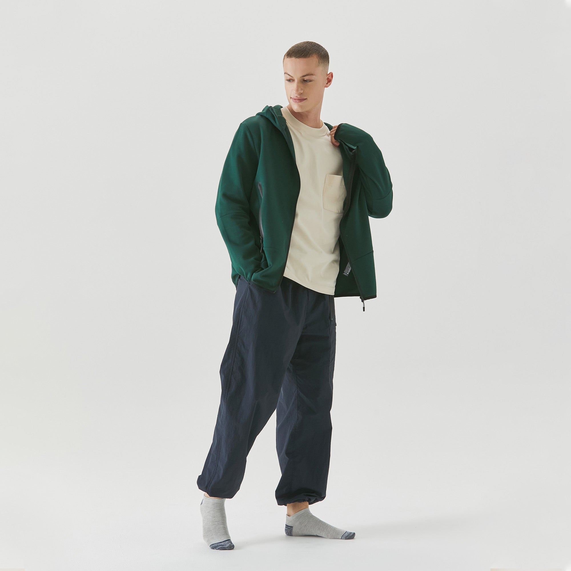 A man in a green jacket is standing with his hands in his pockets.