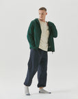 A man in a green jacket is standing with his hands in his pockets.