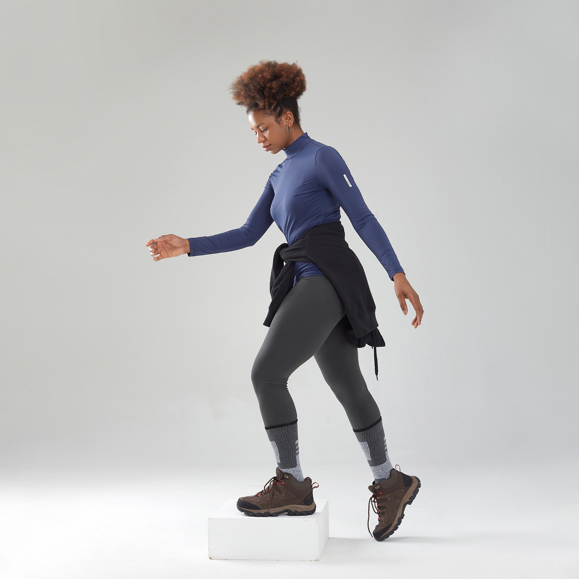 A woman in a blue top is standing on a white block.