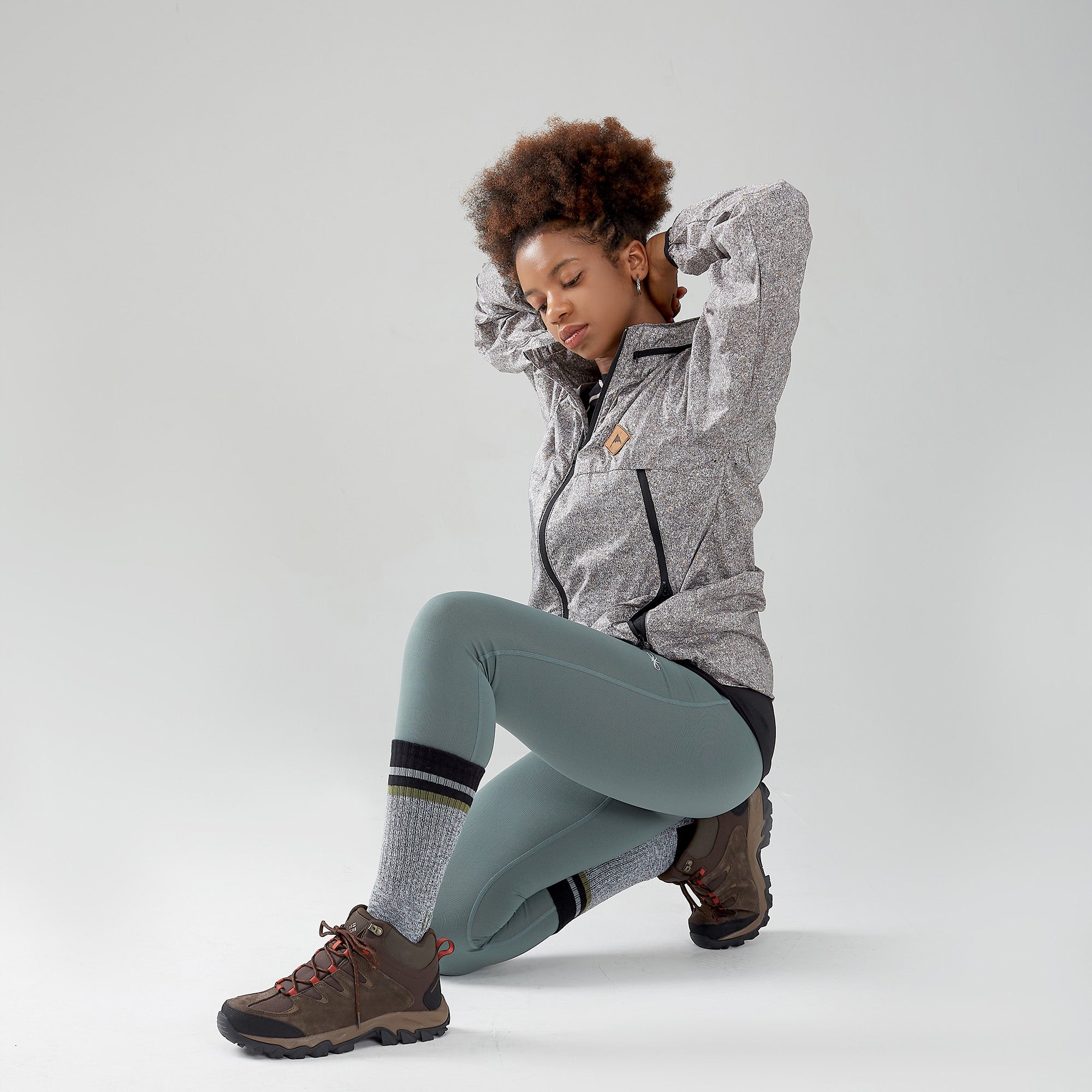 A woman in grey jacket and leggings sitting on the ground.