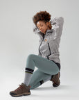 A woman in grey jacket and leggings sitting on the ground.