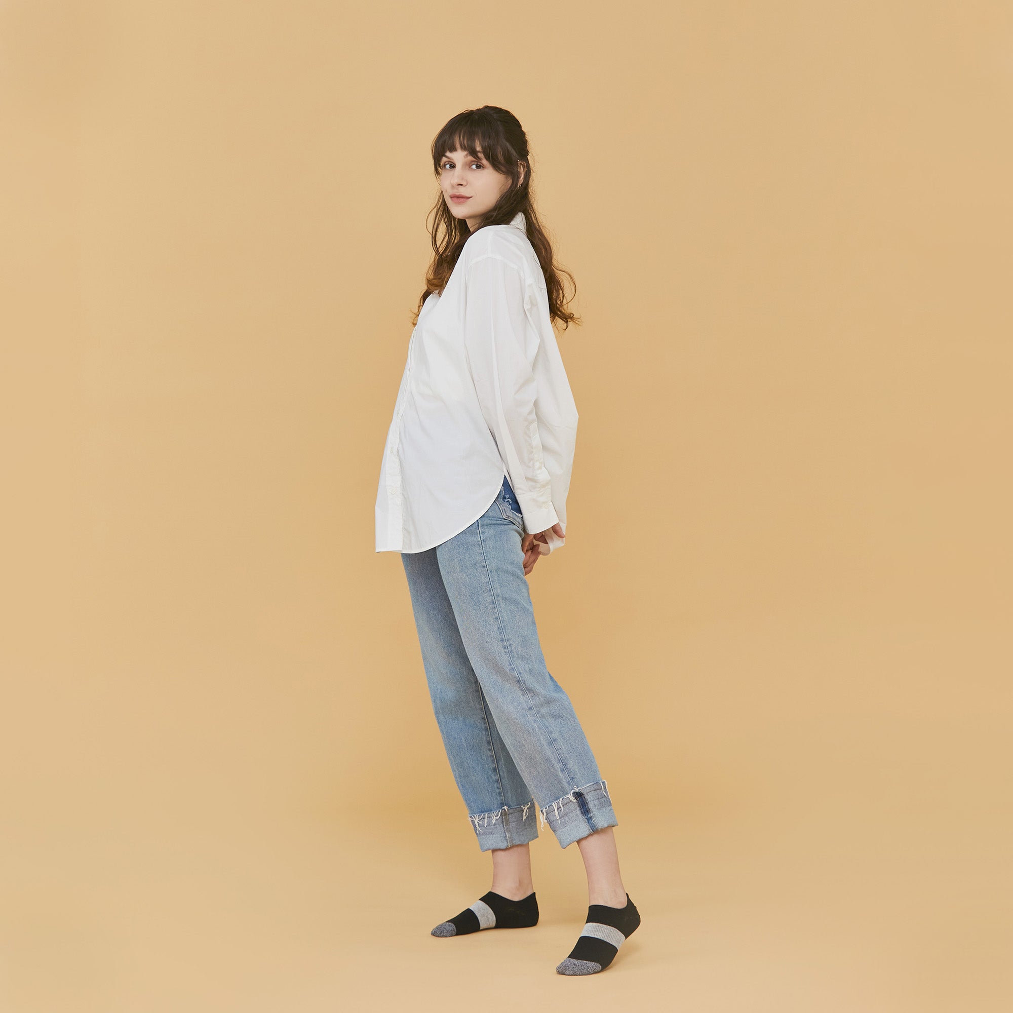 A woman standing in front of a tan background.