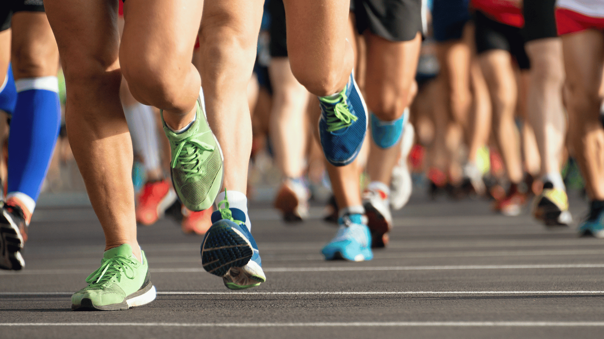 Close-up of runners' legs and shoes on a road during a race or marathon event.