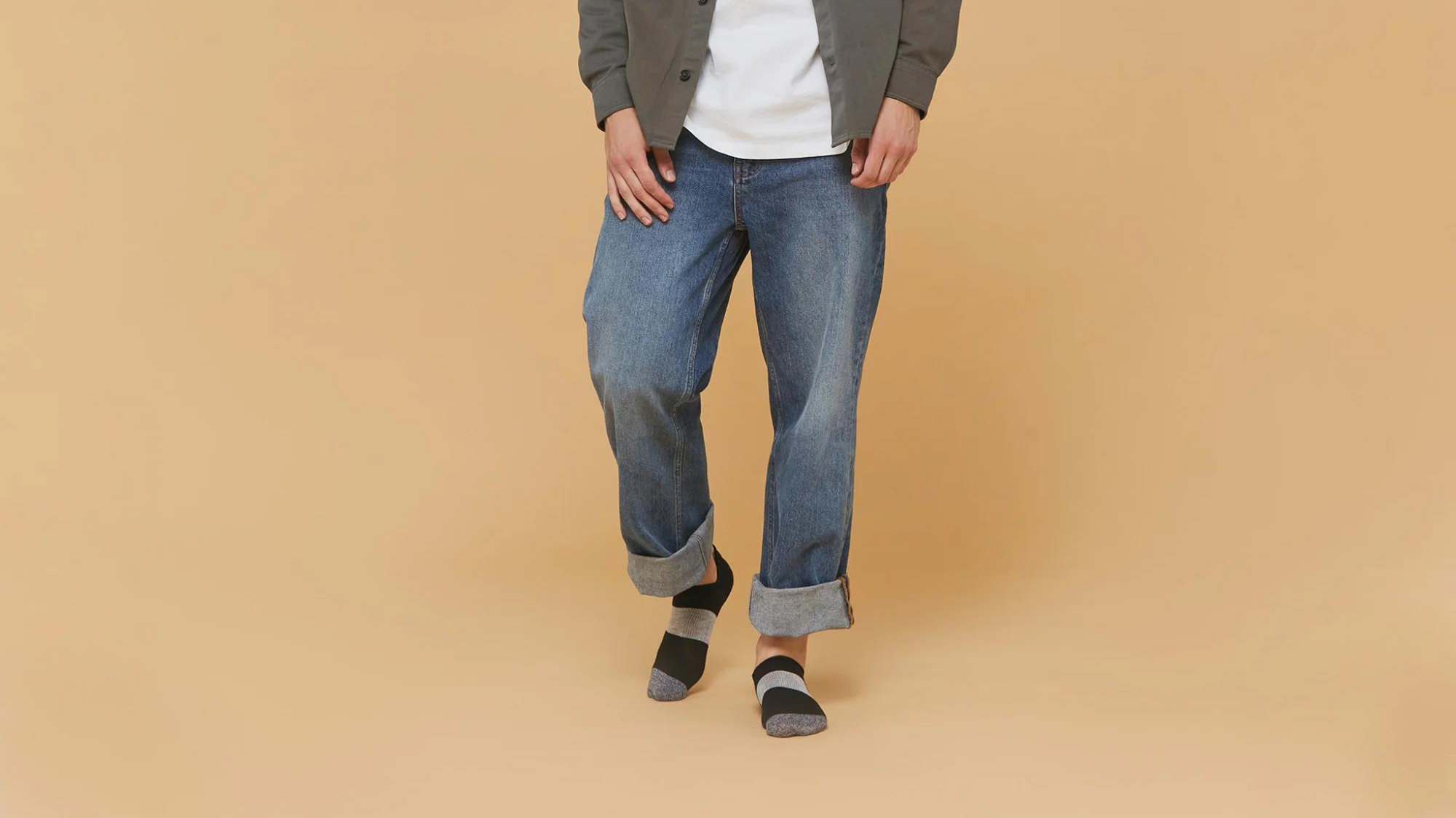 Close-up of a person wearing rolled-up blue jeans, showing off their stylish black, grey, and white socks on a beige background. Perfect for casual outfit inspiration