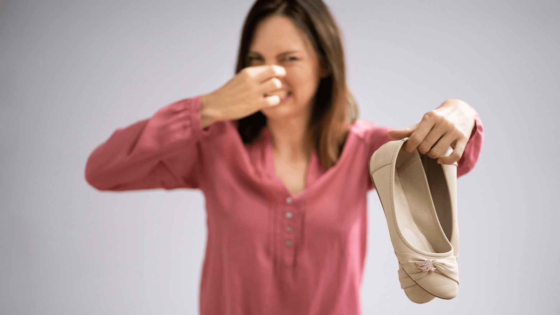 woman holding up shoes and holding her nose, expressing how stinky the shoes are.